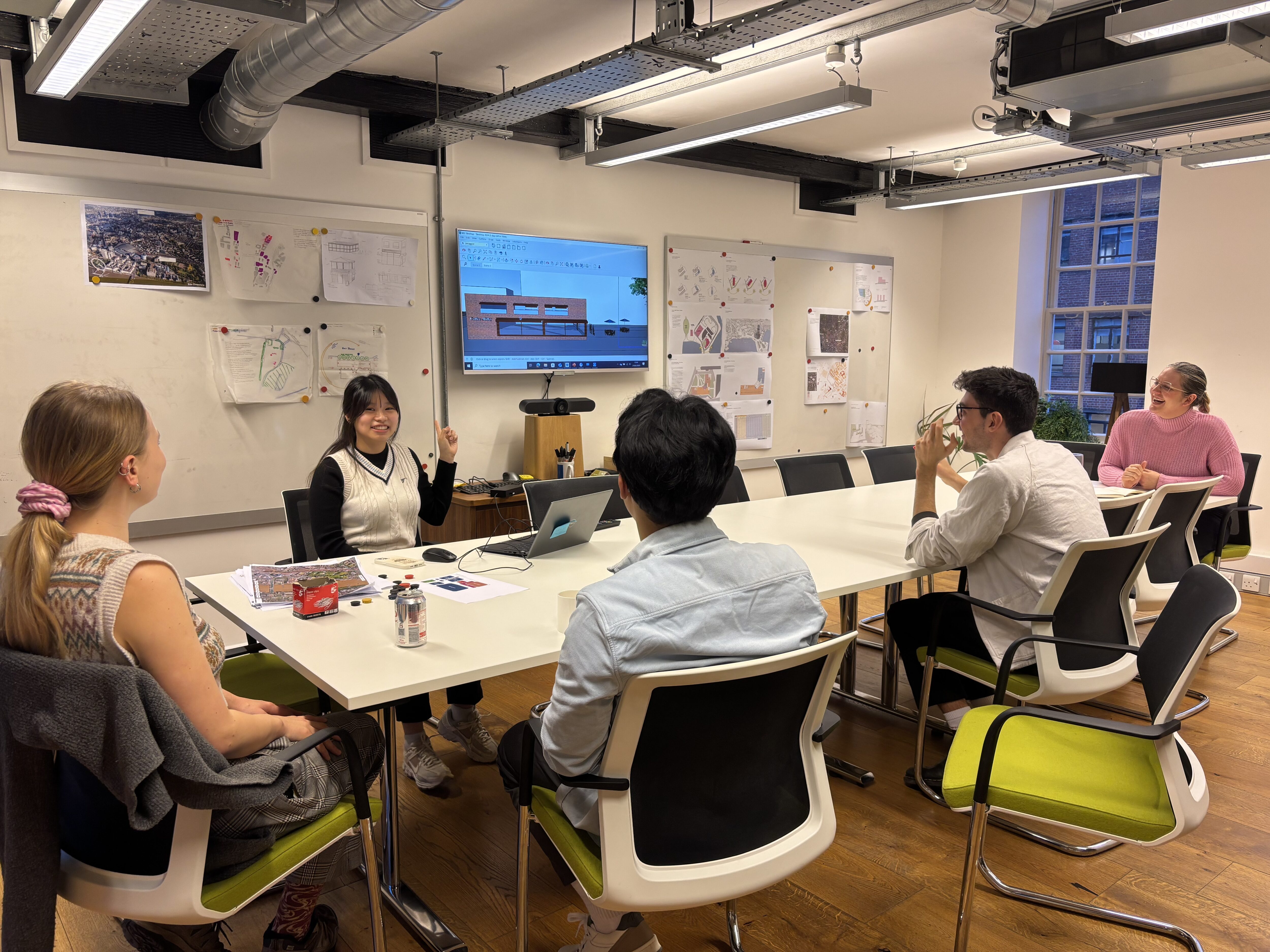 Staff in the London studio meeting room, sat round a table, watching a presentation.